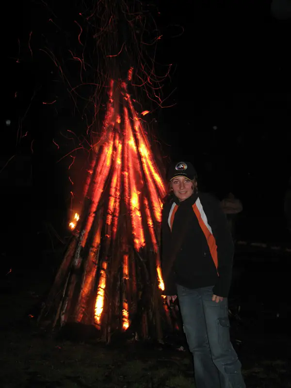Camper posing in front of a burning log teepee at night