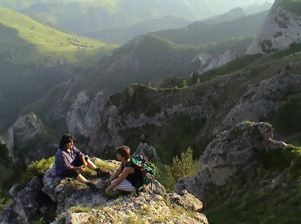 Two hikers resting on a rocky outcrop above a green mountain valley