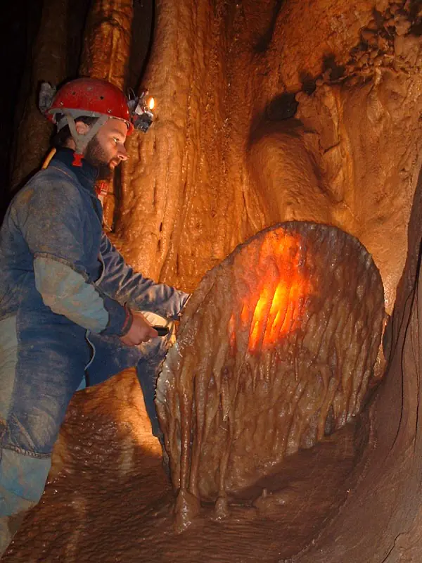 Caver in a red helmet lighting a translucent calcite drapery