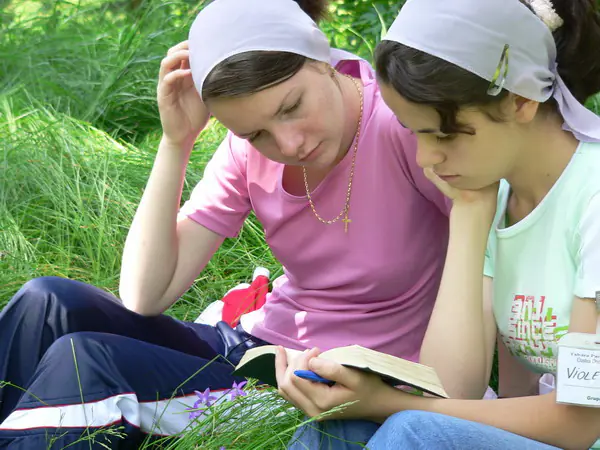 Two girls in headscarves reading the Bible together on the grass