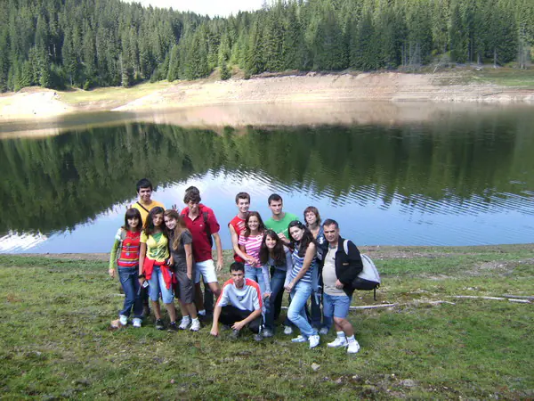 Group of teenagers posing on the lakeshore with the forest reflected in the water