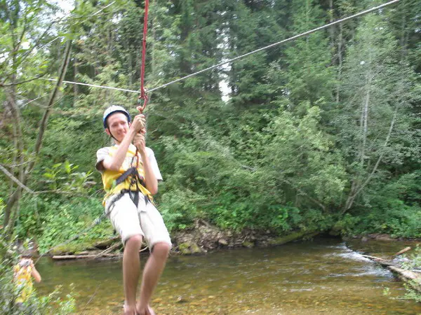 Young man in a harness riding the zip line over a forest stream