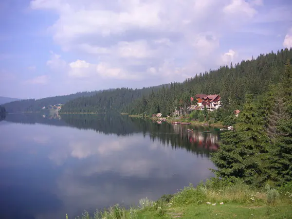 Calm Lake Beliș–Fântânele reflecting the clouds, with a guesthouse on the forested shore
