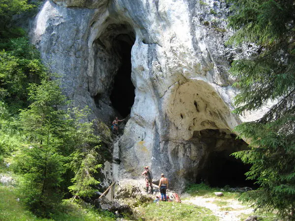 Visitors at the foot of the limestone cliff with the entrances of Humpleului Cave